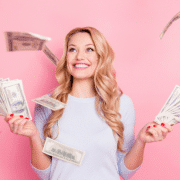 young blonde woman holding money against pink wall