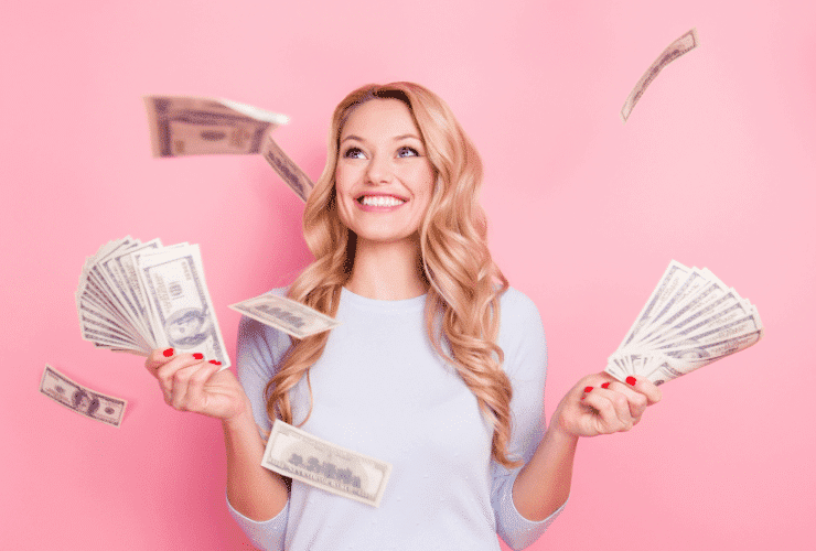 young blonde woman holding money against pink wall