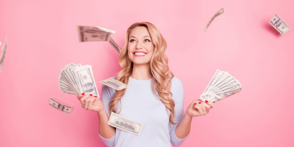 young blonde woman holding money against pink wall